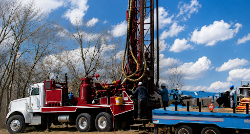 Johnston Water Wells drilling rig truck on an active job site in Walker County, TX — crew operating tall drill mast under a blue sky